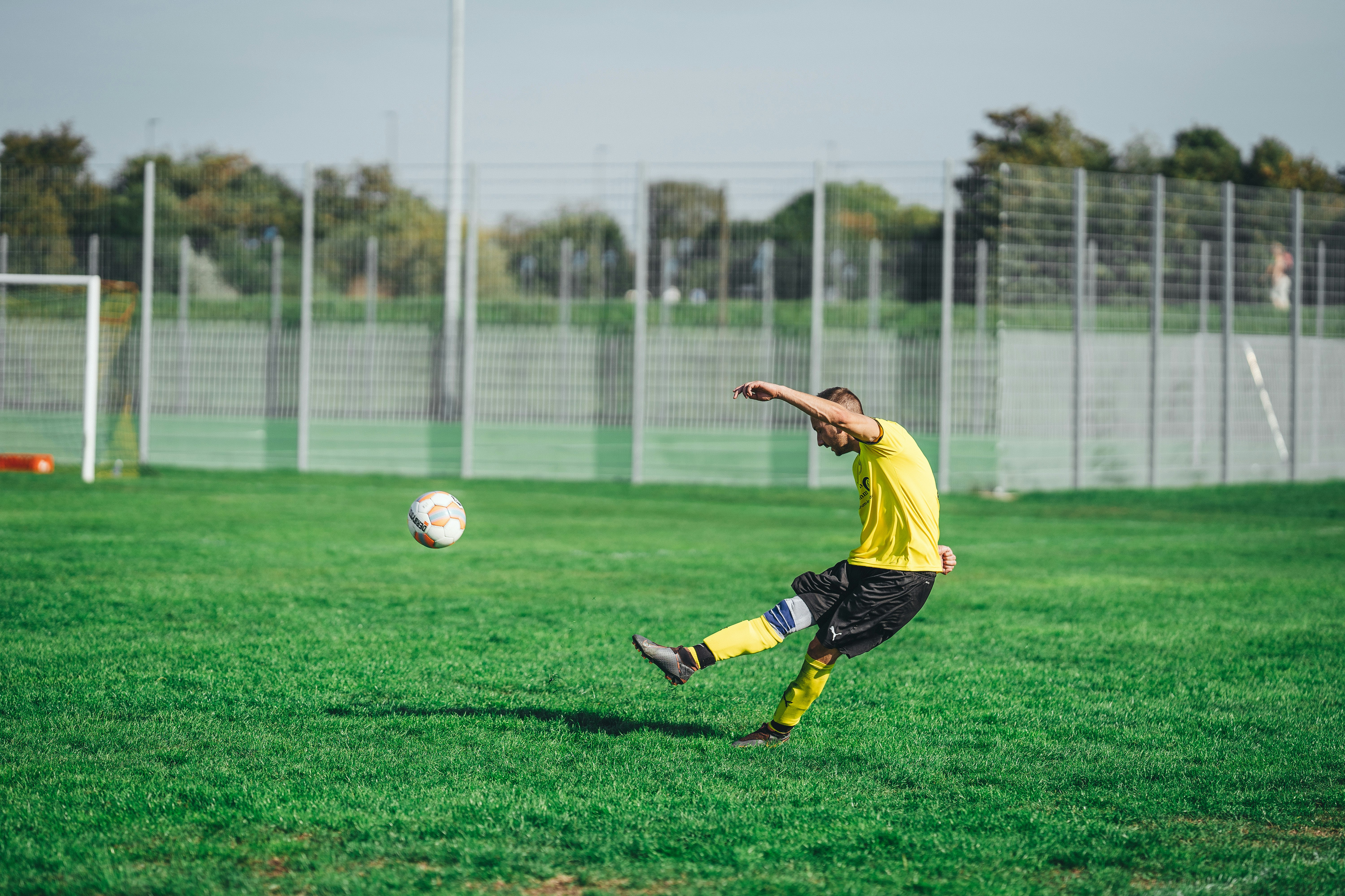 man in yellow shirt and black shorts playing soccer during daytime